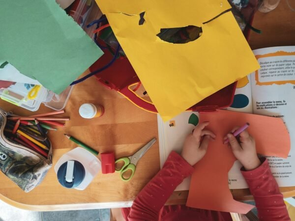 Un enfant qui dessine sur un papier orange, entouré de matériel de bricolage